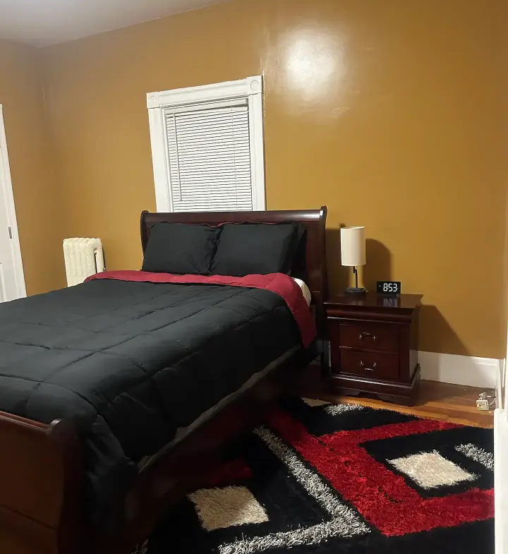 A bedroom with a bed, nightstand and window.