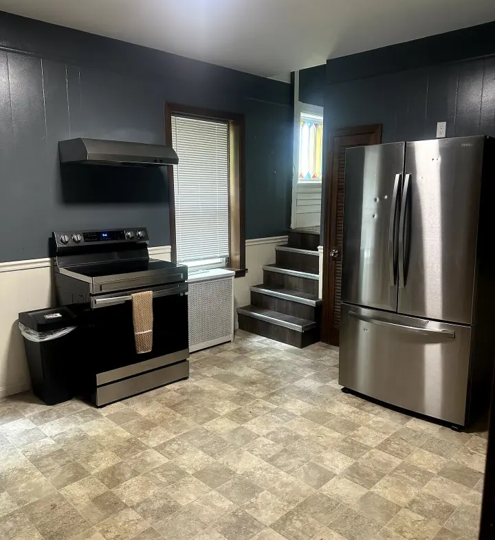 A kitchen with a stove, refrigerator and stairs.