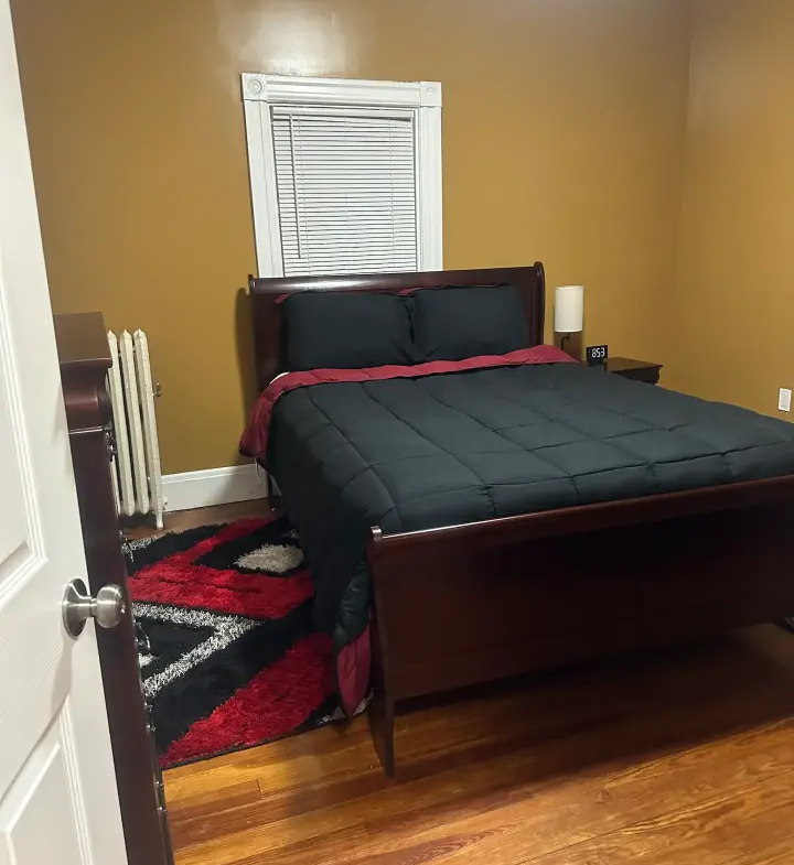 A bedroom with a bed, nightstand and window.