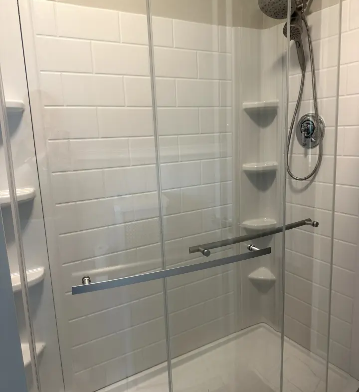 A white tiled shower with glass doors and shelves.