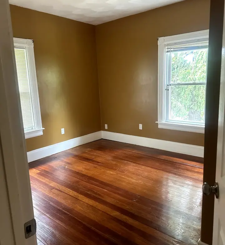 A room with wood floors and two windows.