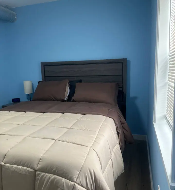 A bed room with a neatly made bed and blue walls