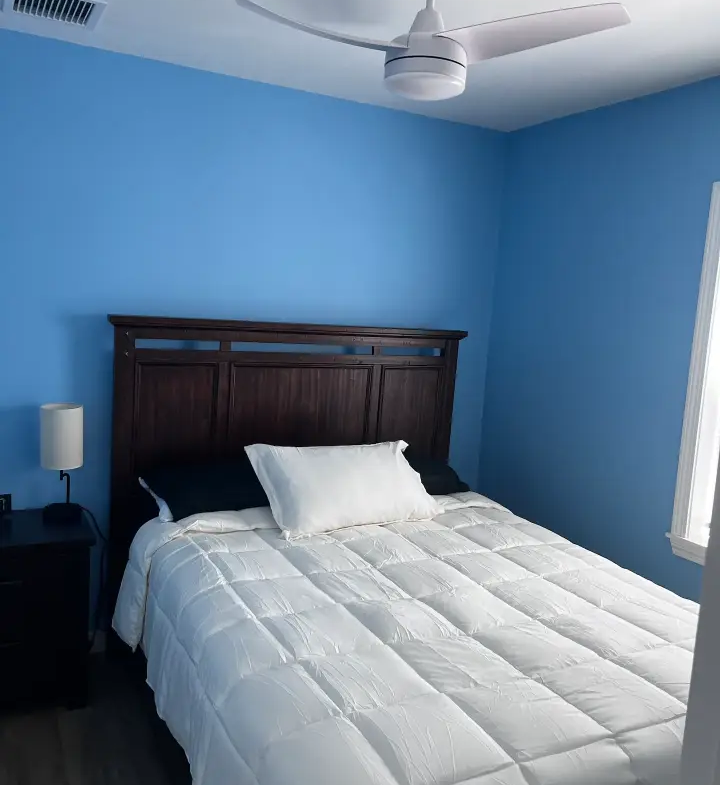 A bedroom with blue walls and white bedding.