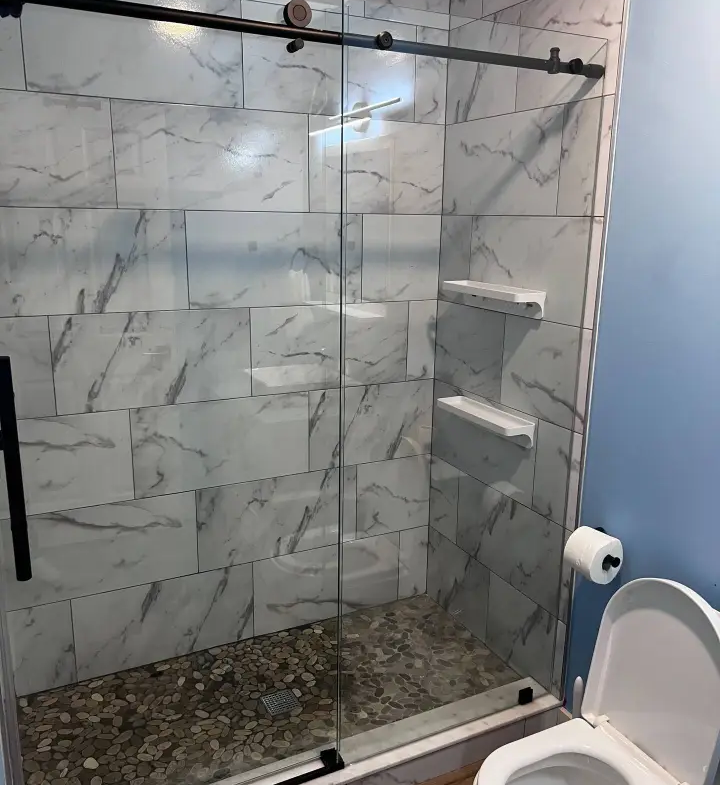 A bathroom with marble walls and floor, and a glass shower door.