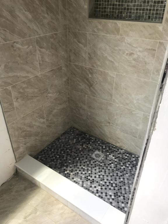 A shower with a tiled floor and a white tile wall.